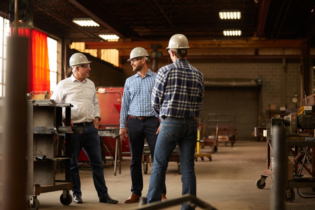 Three warehouse workers talking in white hard hats on warehouse floor